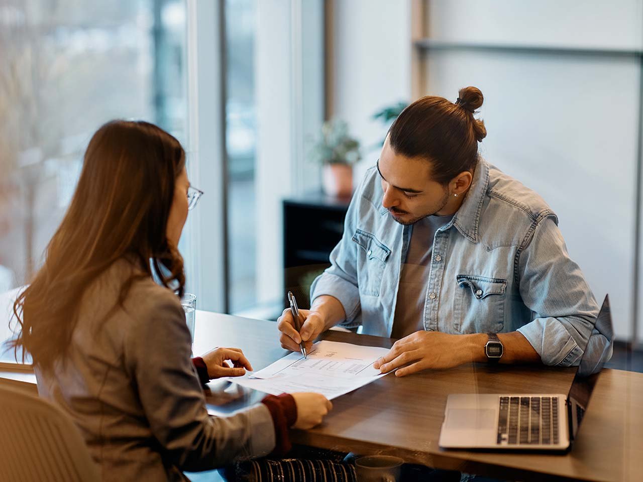 Young Hispanic man signing loan agreement during meeting with his bank manager in office.