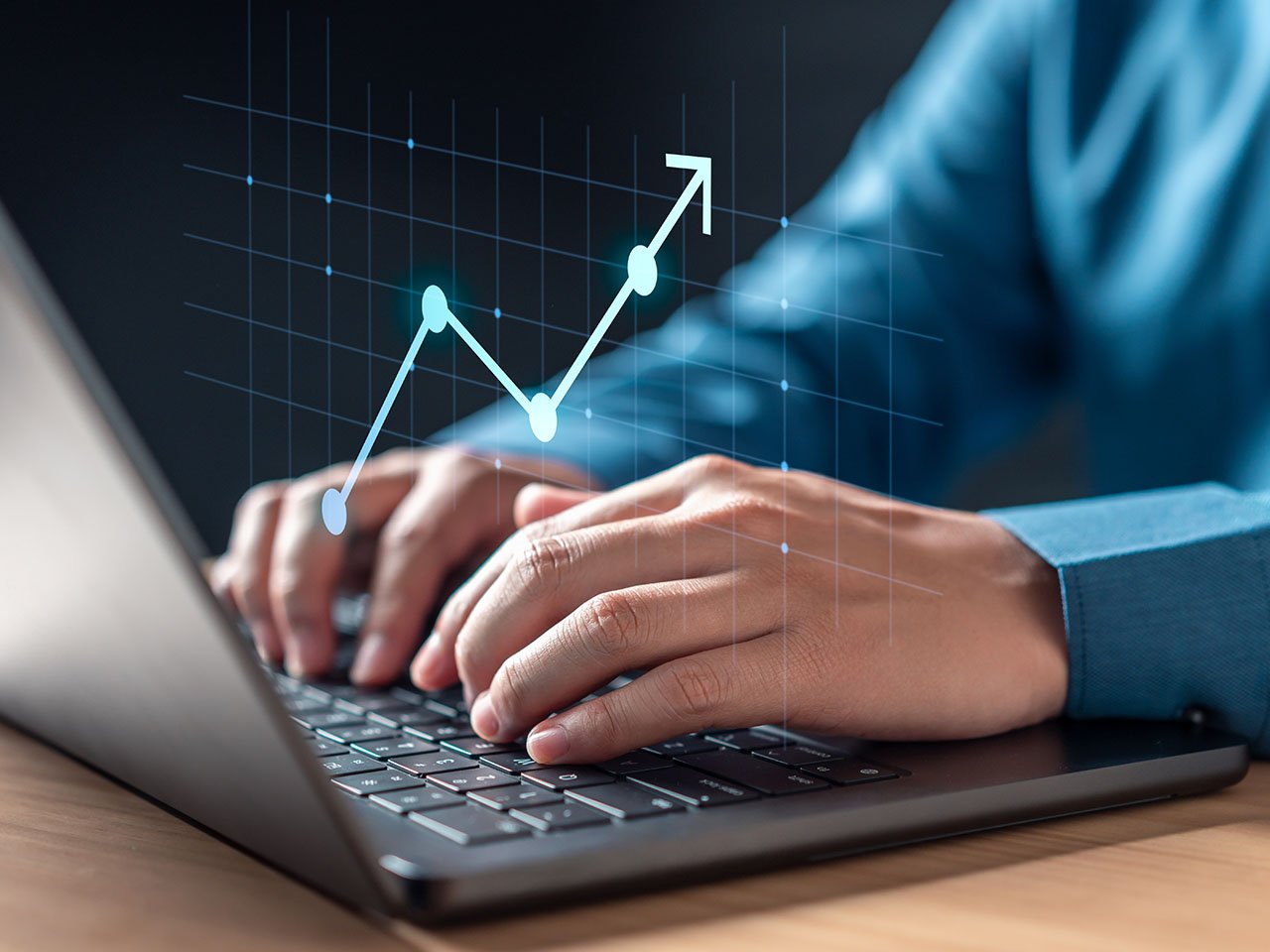 A person is typing on a laptop with a graph of a line going up.